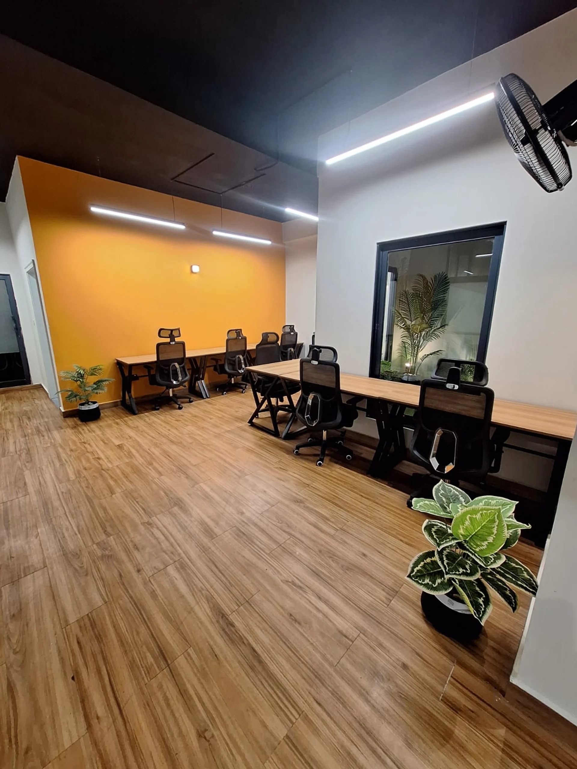 Open coworking hall at Panda Works in PCSIR Phase 2, Lahore, with an orange accent wall and ergonomic chairs